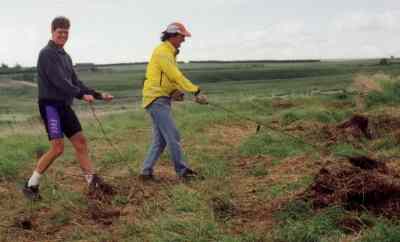 Guido (L) and Jeff extricate rusty barb wire out of thick grass.